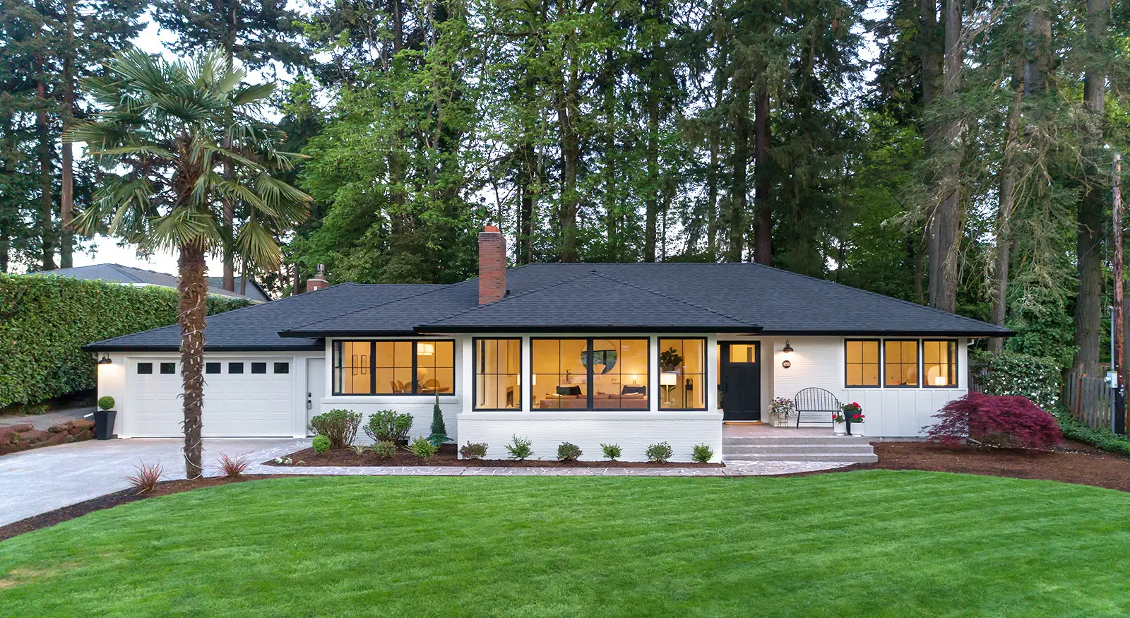 Hemlock home after the whole-home remodel: white-painted brick, black roof, and black-framed windows at dusk