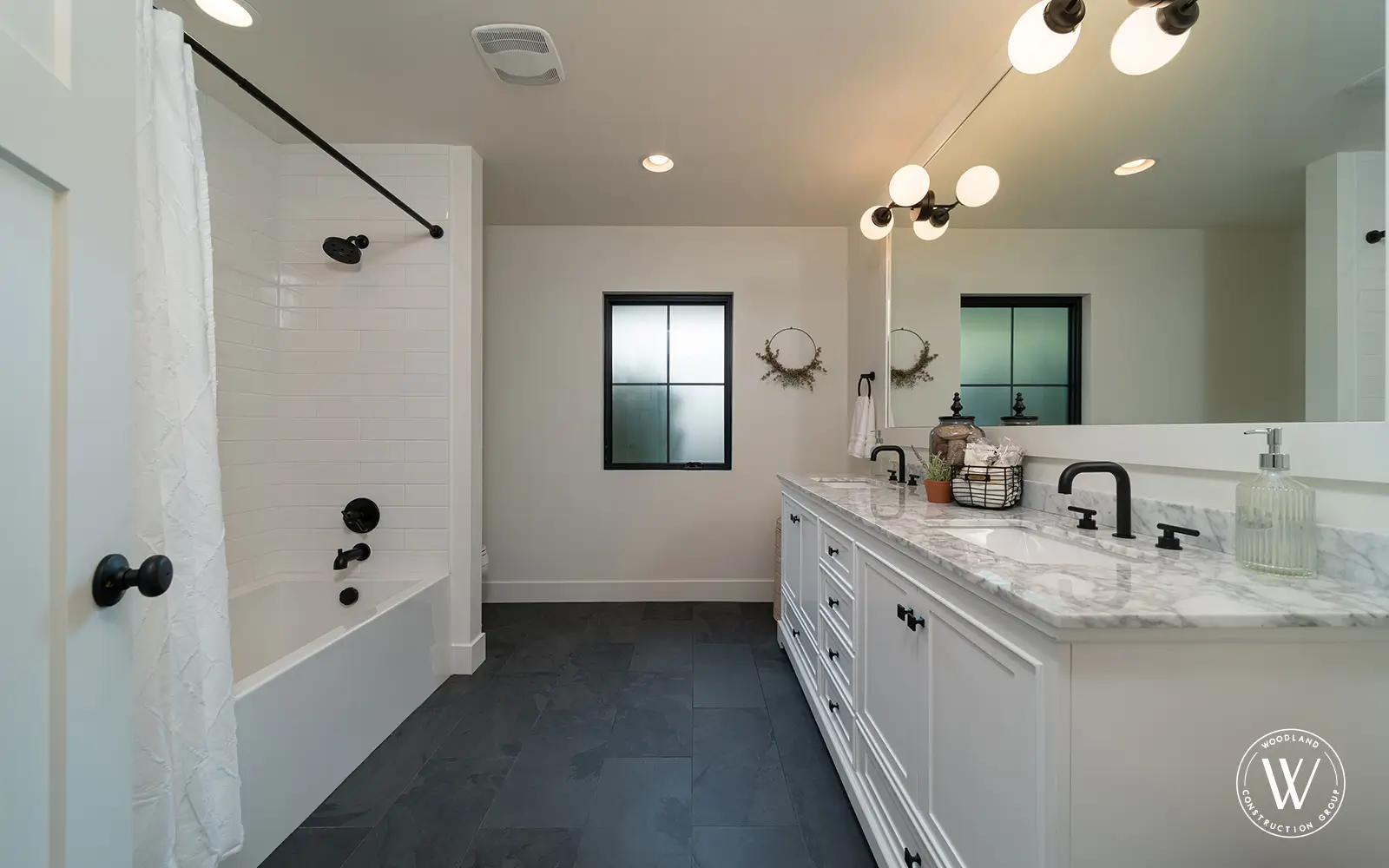 Hemlock primary bath after: white subway tile tub surround, marble-top double vanity, slate floor and black fixtures