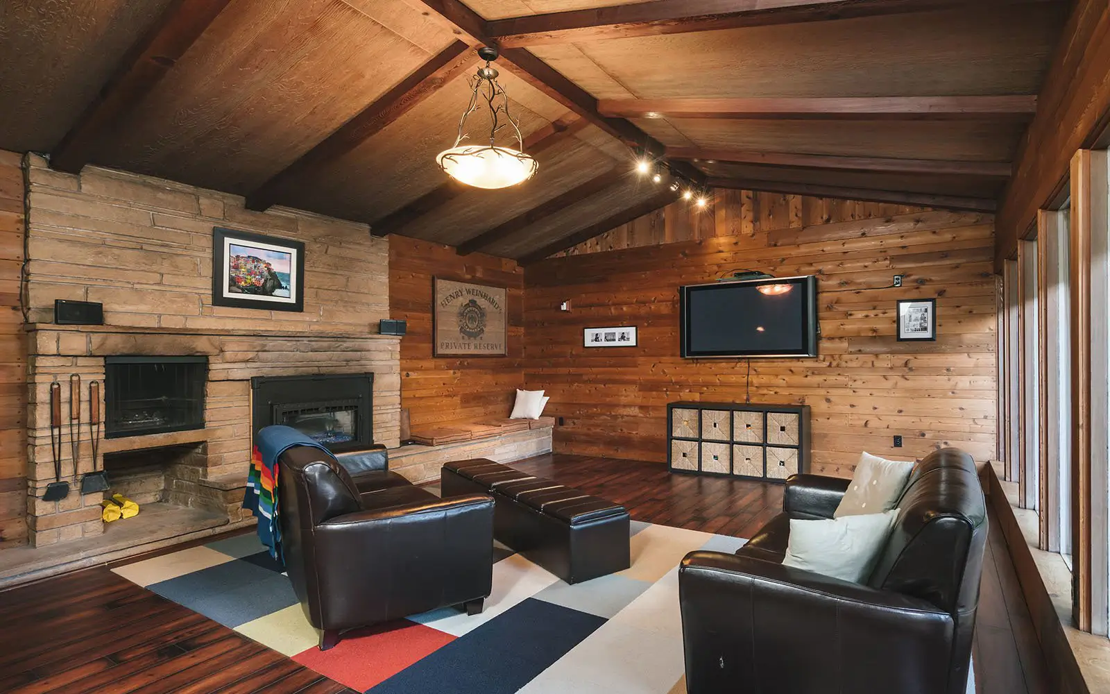 Hemlock den before: dark cedar-paneled room with a stone fireplace and vaulted wood ceiling