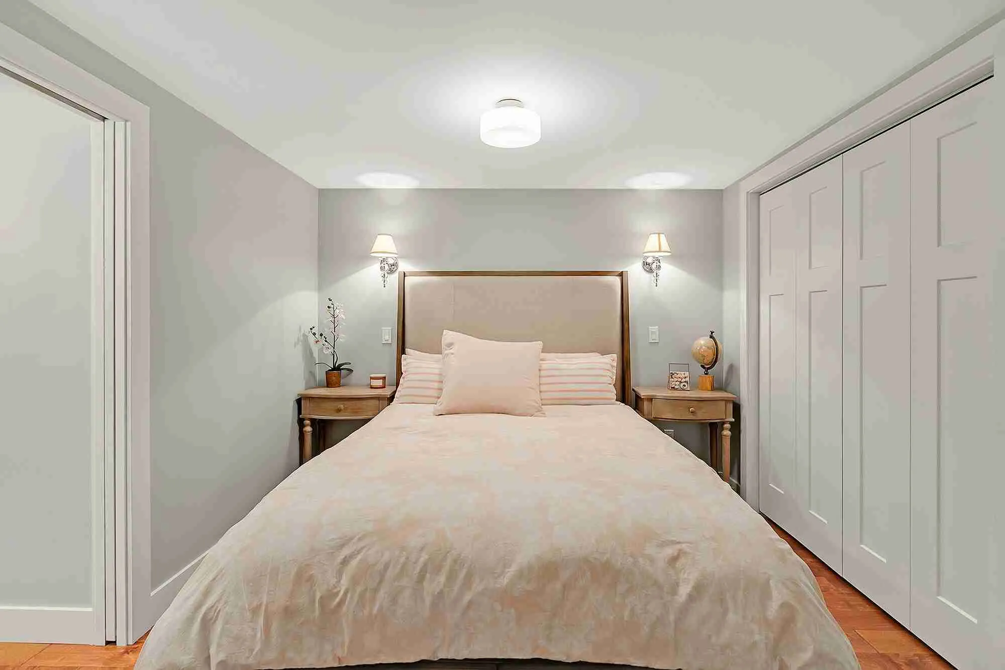 Second finished Hemlock basement bedroom with soft grey walls, paired wall sconces and hardwood flooring
