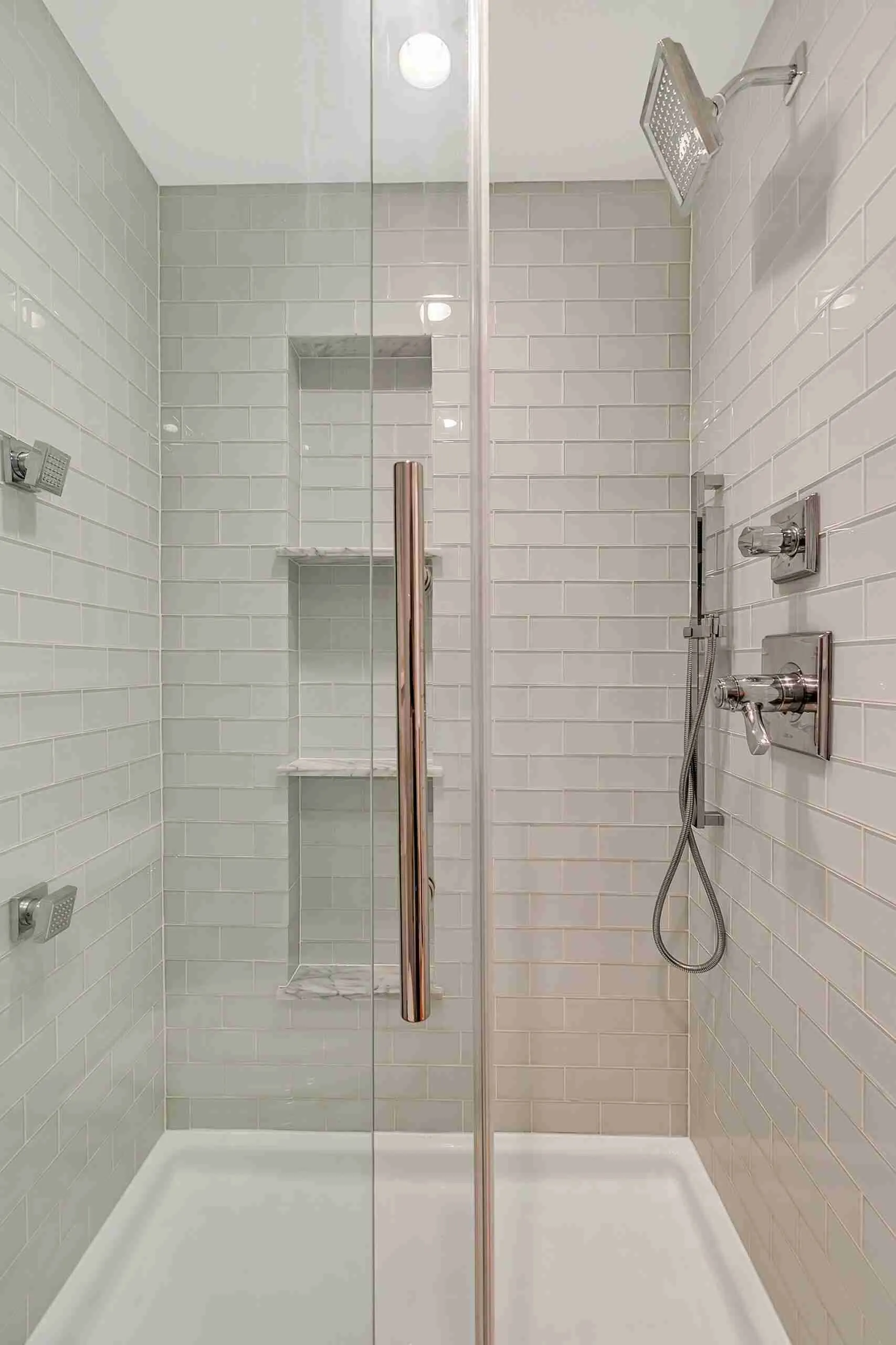 Hemlock basement full bath with a glass walk-in shower, pale subway tile, marble niche shelves and a rain shower head