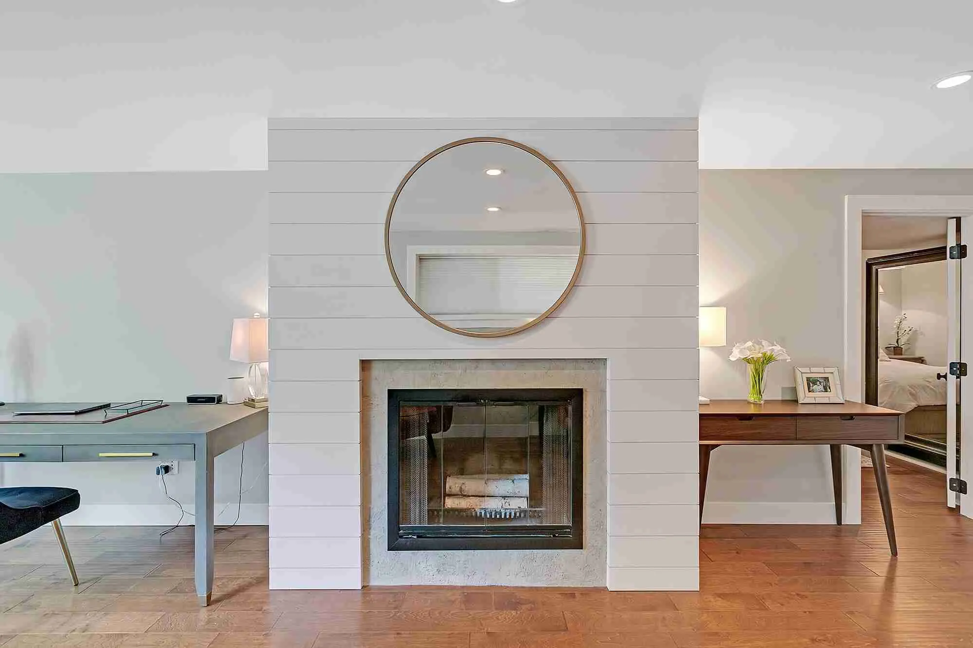 Hemlock basement fireplace clad in white shiplap with a round mirror, flanked by a desk nook and a bedroom entry
