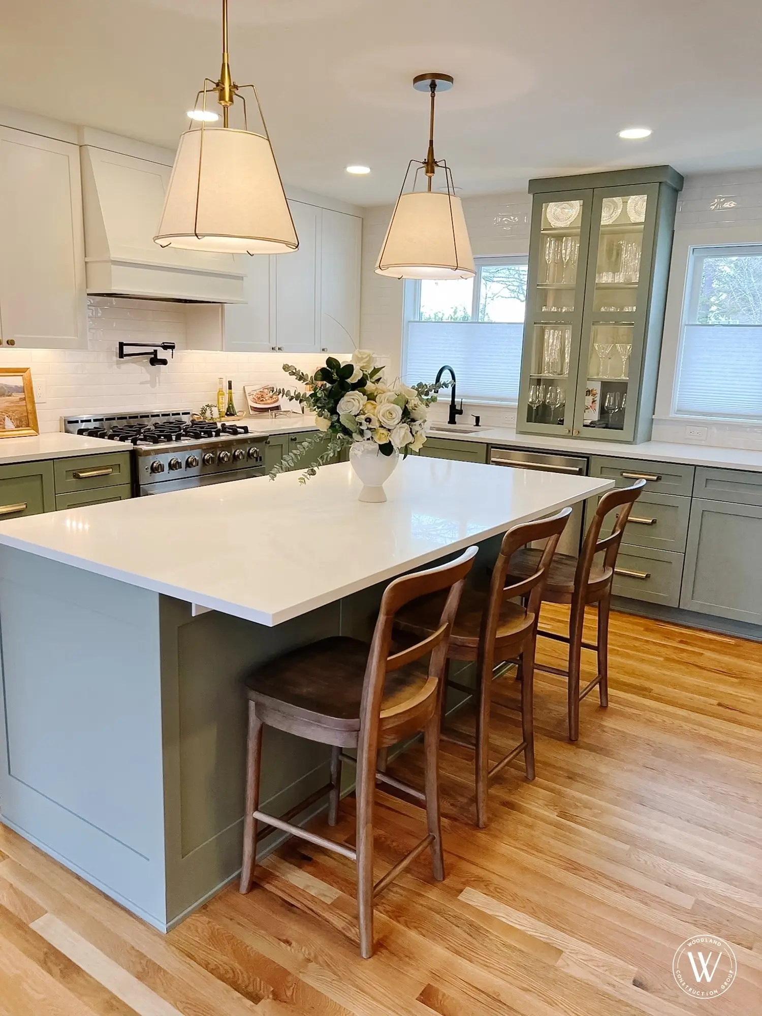 Murray kitchen island with a white quartz top, pendant lighting and wood counter stools, sage-green cabinetry beyond