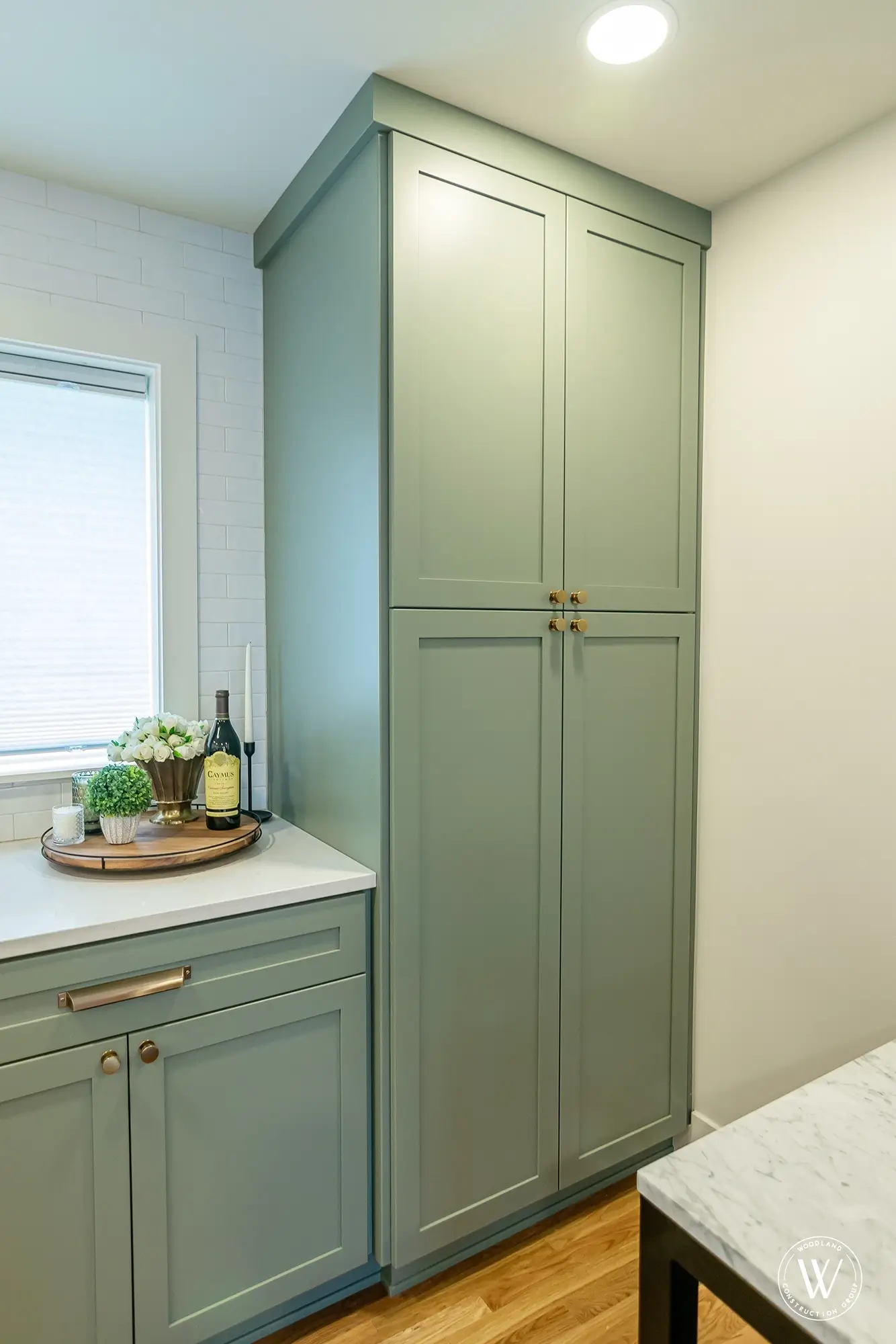 Full-height sage-green pantry cabinet with brass hardware in the Murray kitchen