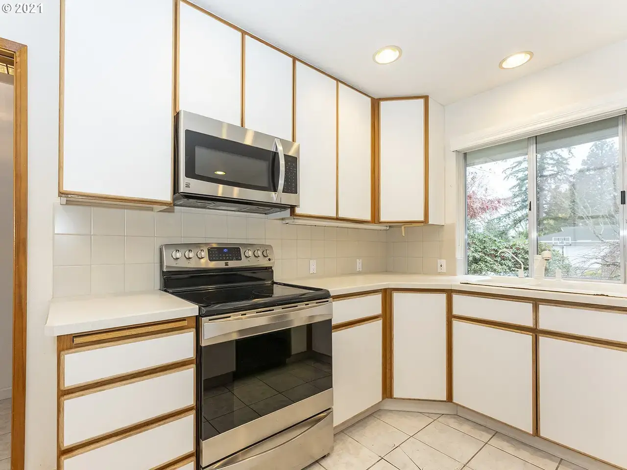 Sherwood range wall before: an electric range, tile counters and dated white-and-oak cabinets