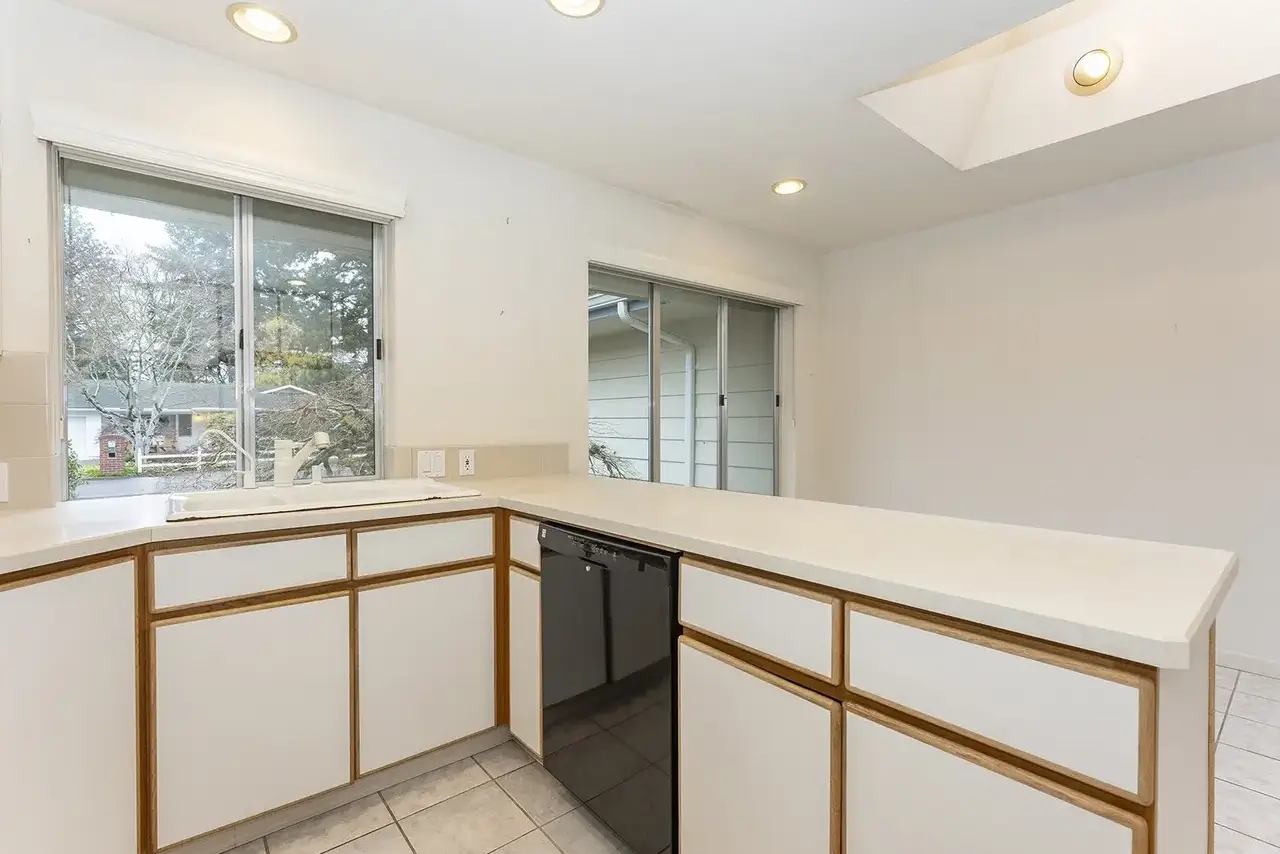 Sherwood sink wall before: white-laminate cabinets, tile counters and a black dishwasher