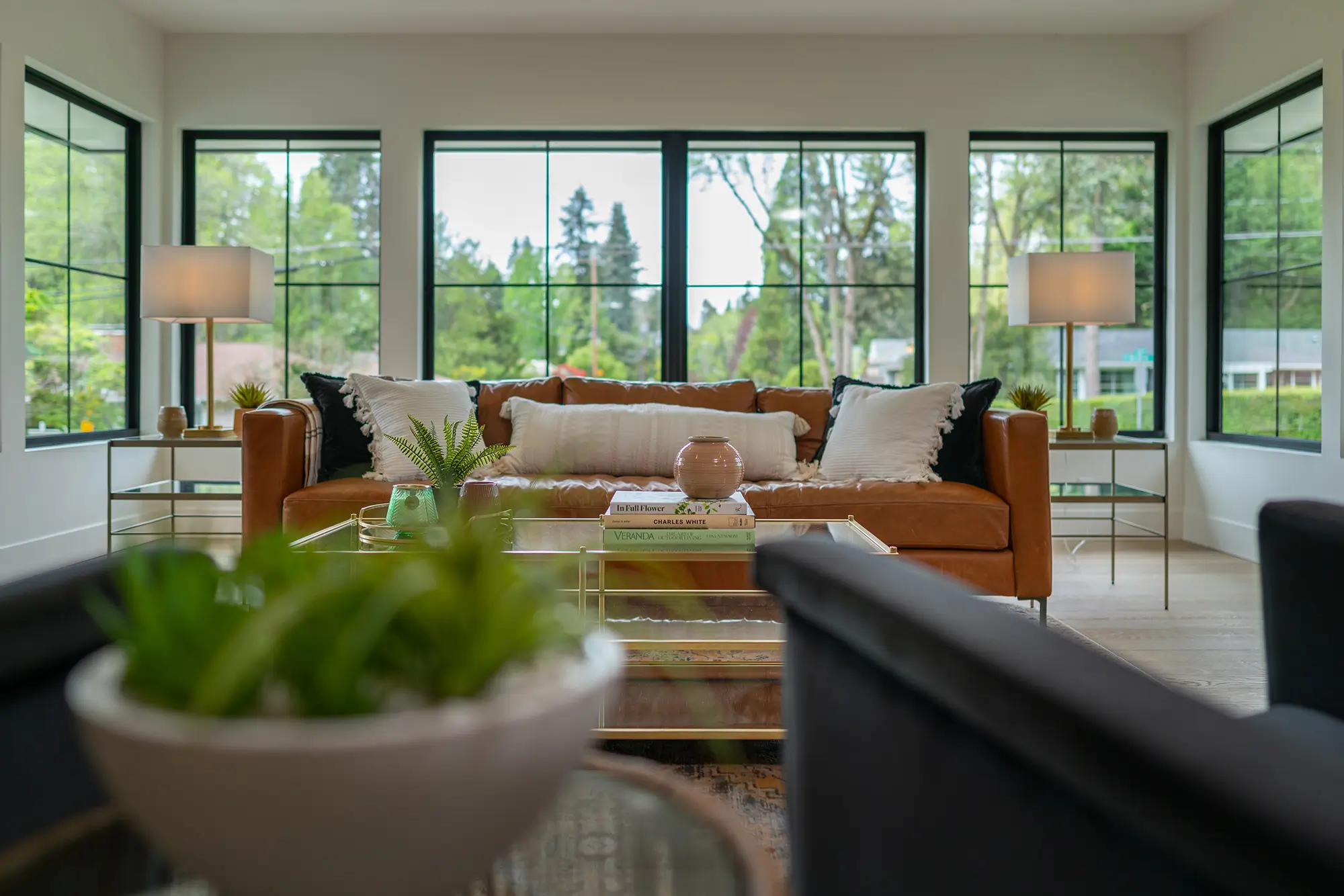 Whitepine living room toward the treed street with a leather sofa, dual lamps and black-framed windows