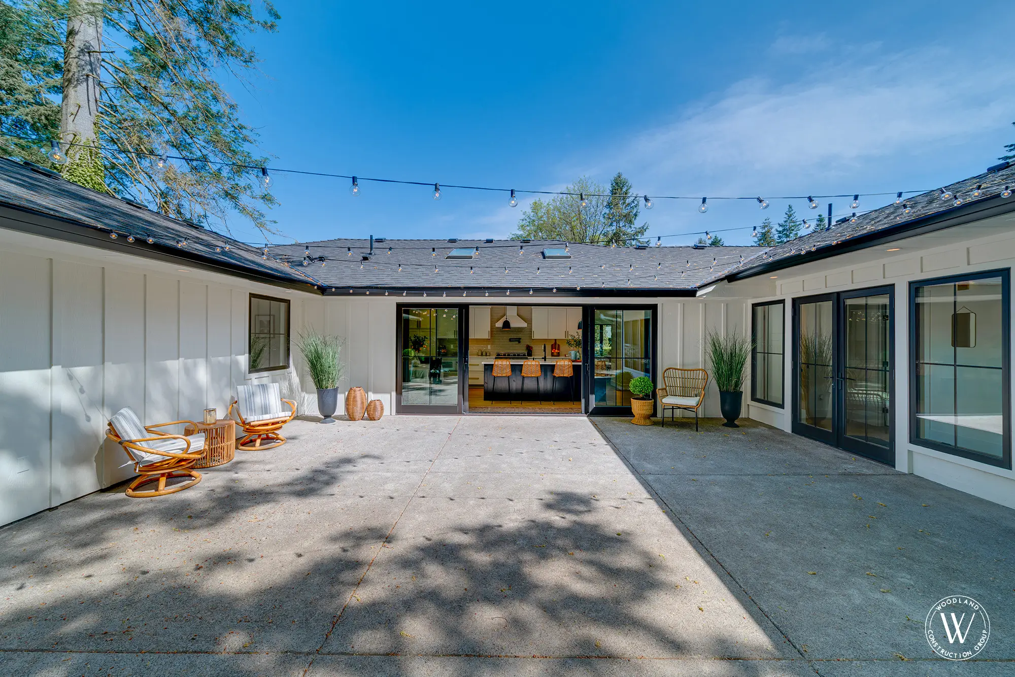Whitepine kitchen opening through 16-foot black sliding doors onto the garden courtyard with string lights