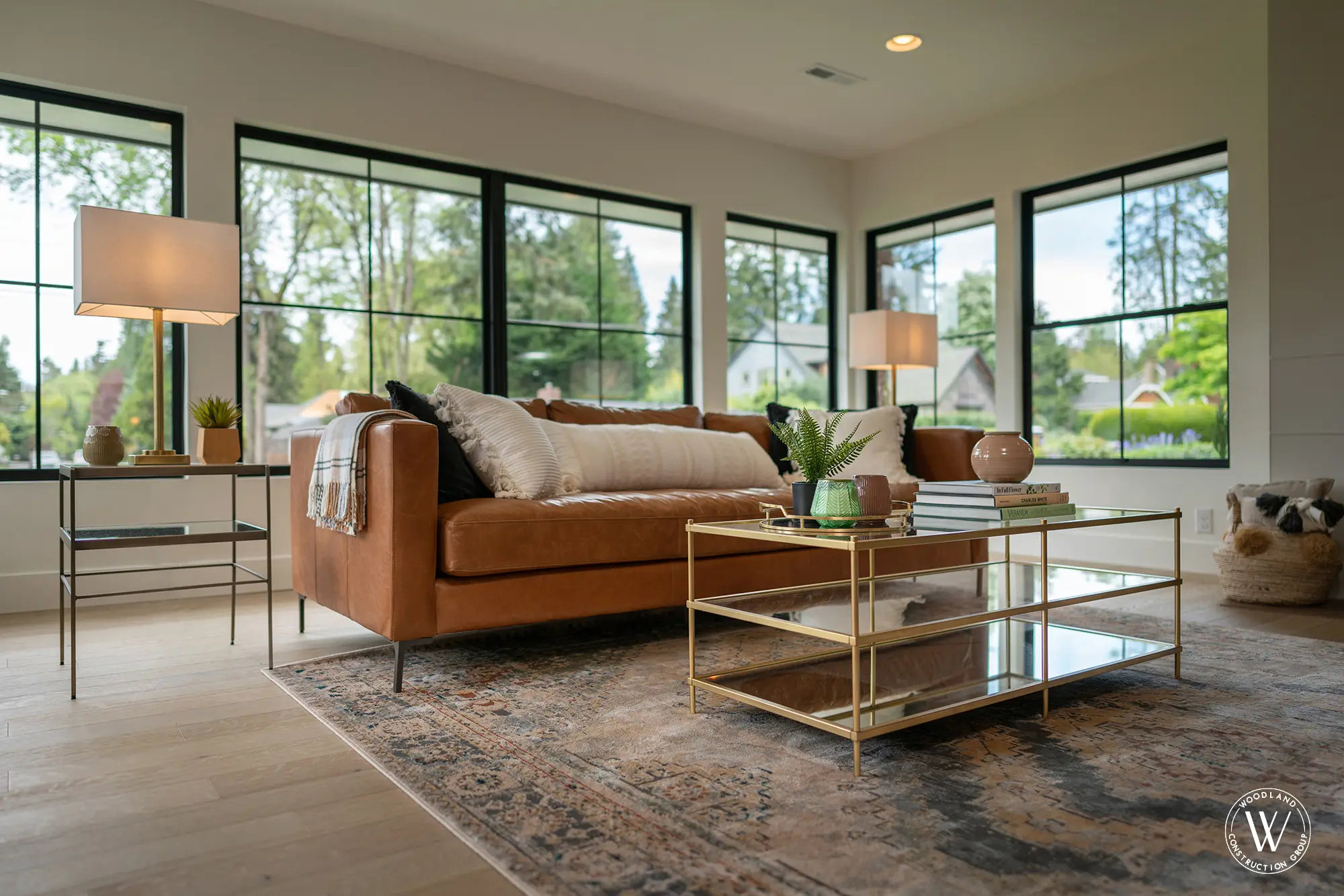 Whitepine living room with a caramel leather sofa and a wall of black-framed windows over the treed West Slope