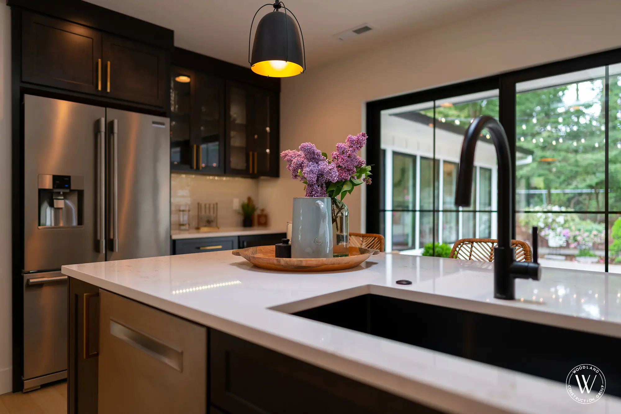 Whitepine kitchen island detail with lilacs and a dark built-in bar wall with a wine refrigerator beyond