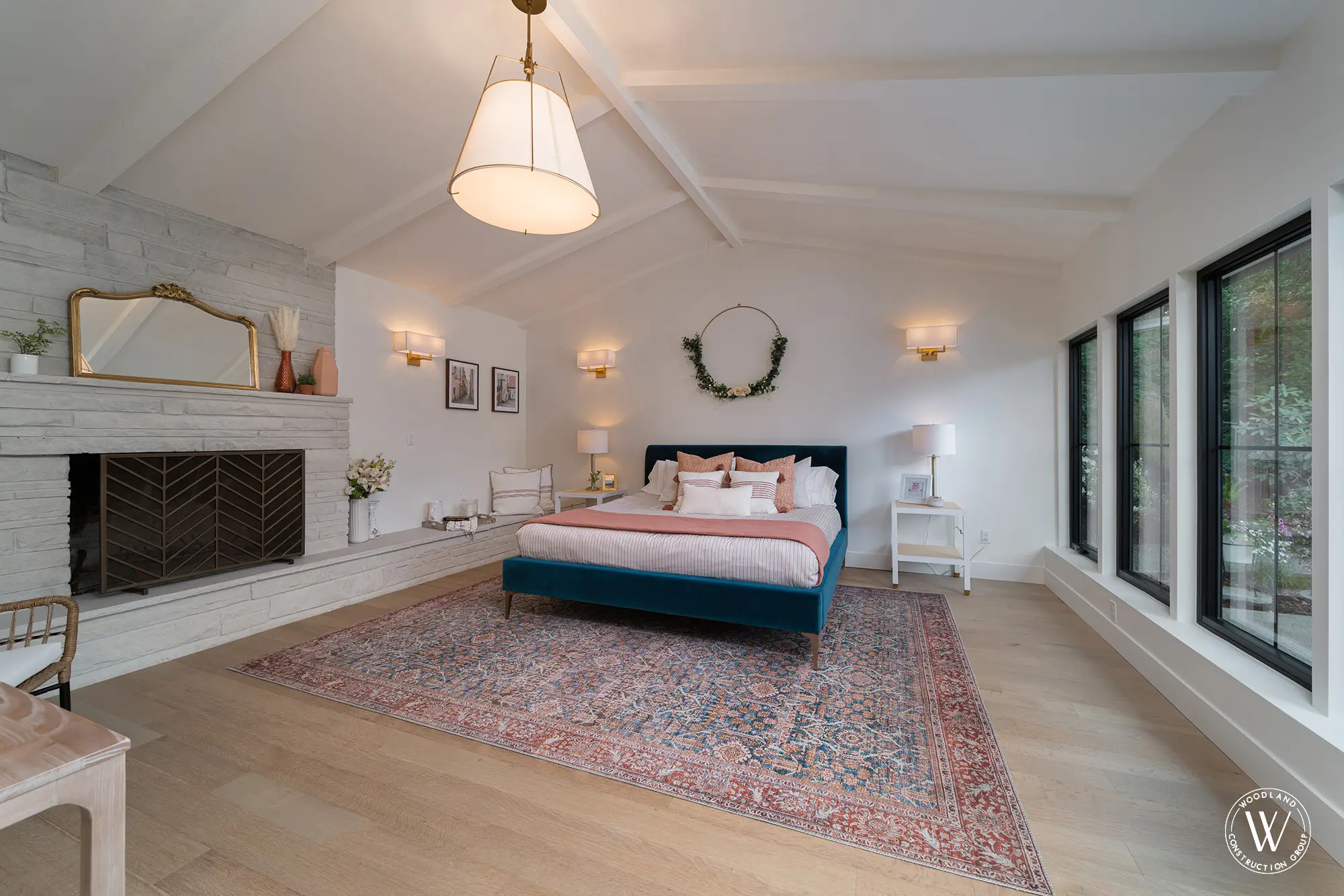 Whitepine primary bedroom under a vaulted, beamed ceiling with a whitewashed stone fireplace and a teal velvet bed