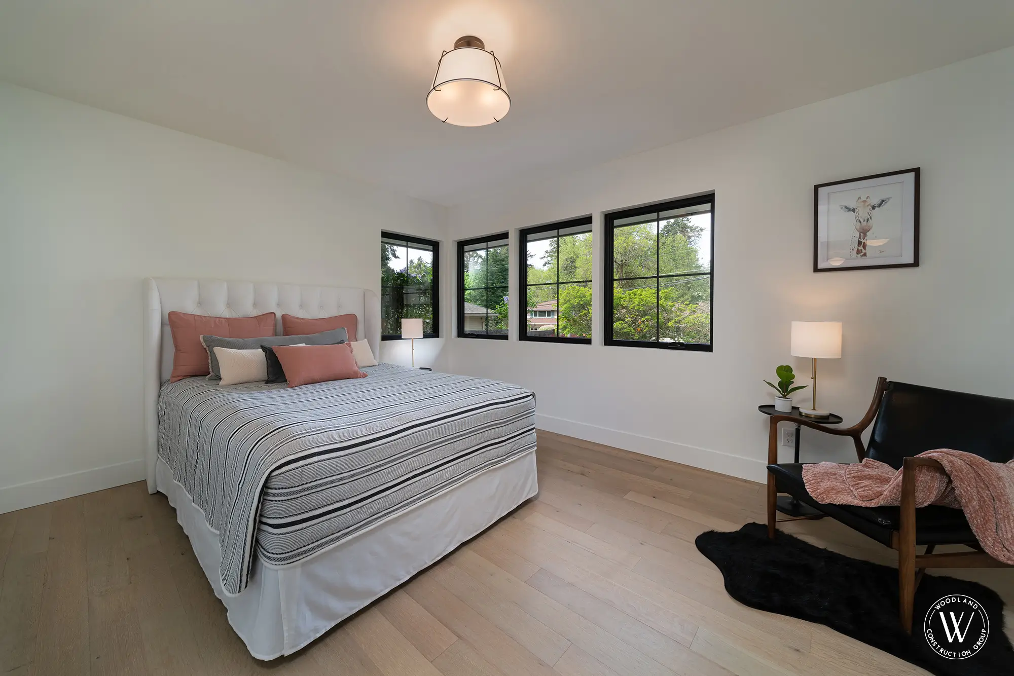 Whitepine guest bedroom with a white tufted headboard, coral pillows and a wall of black-framed garden windows