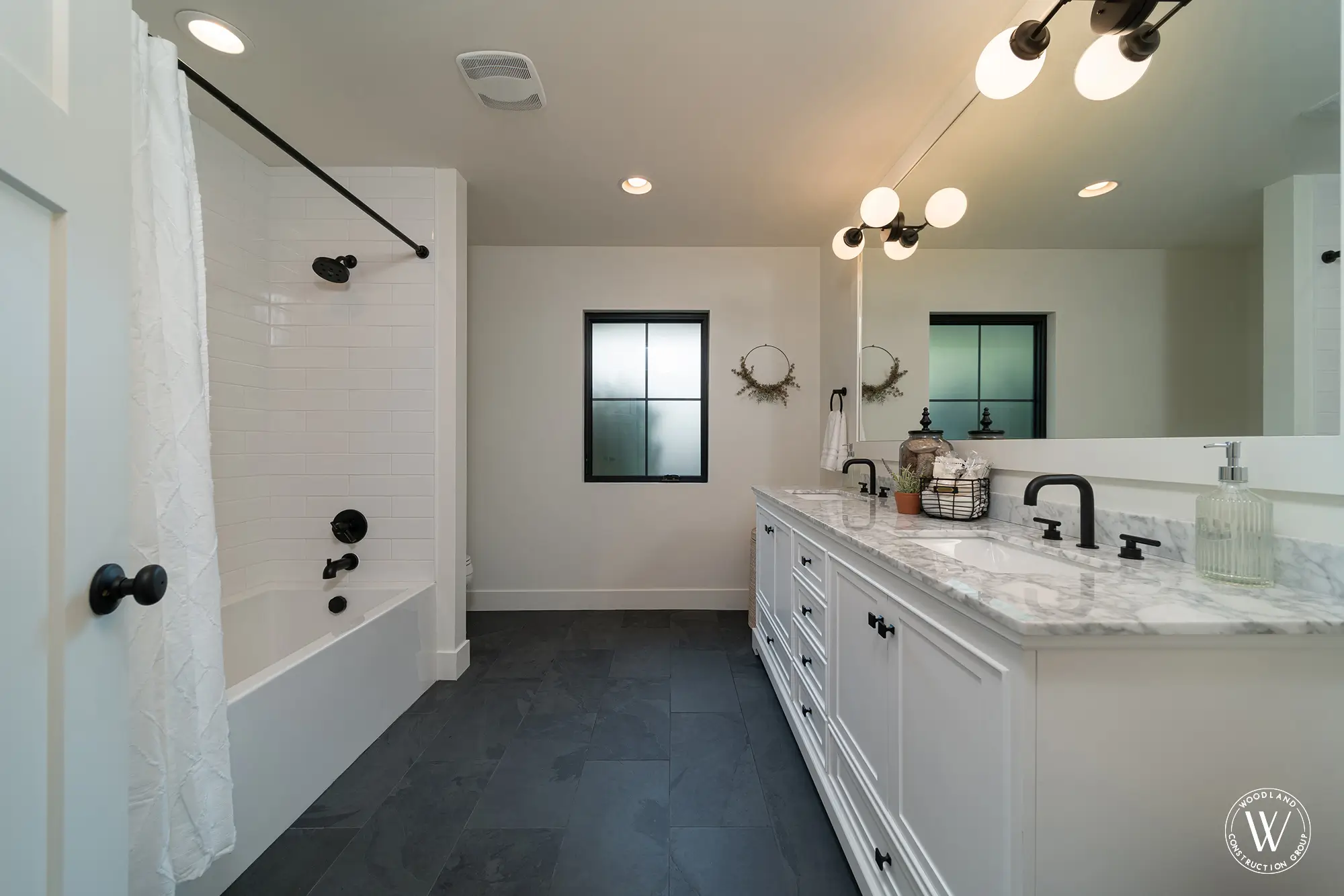 Whitepine hall bath with a white subway-tiled tub and shower, matte-black fixtures and a slate floor
