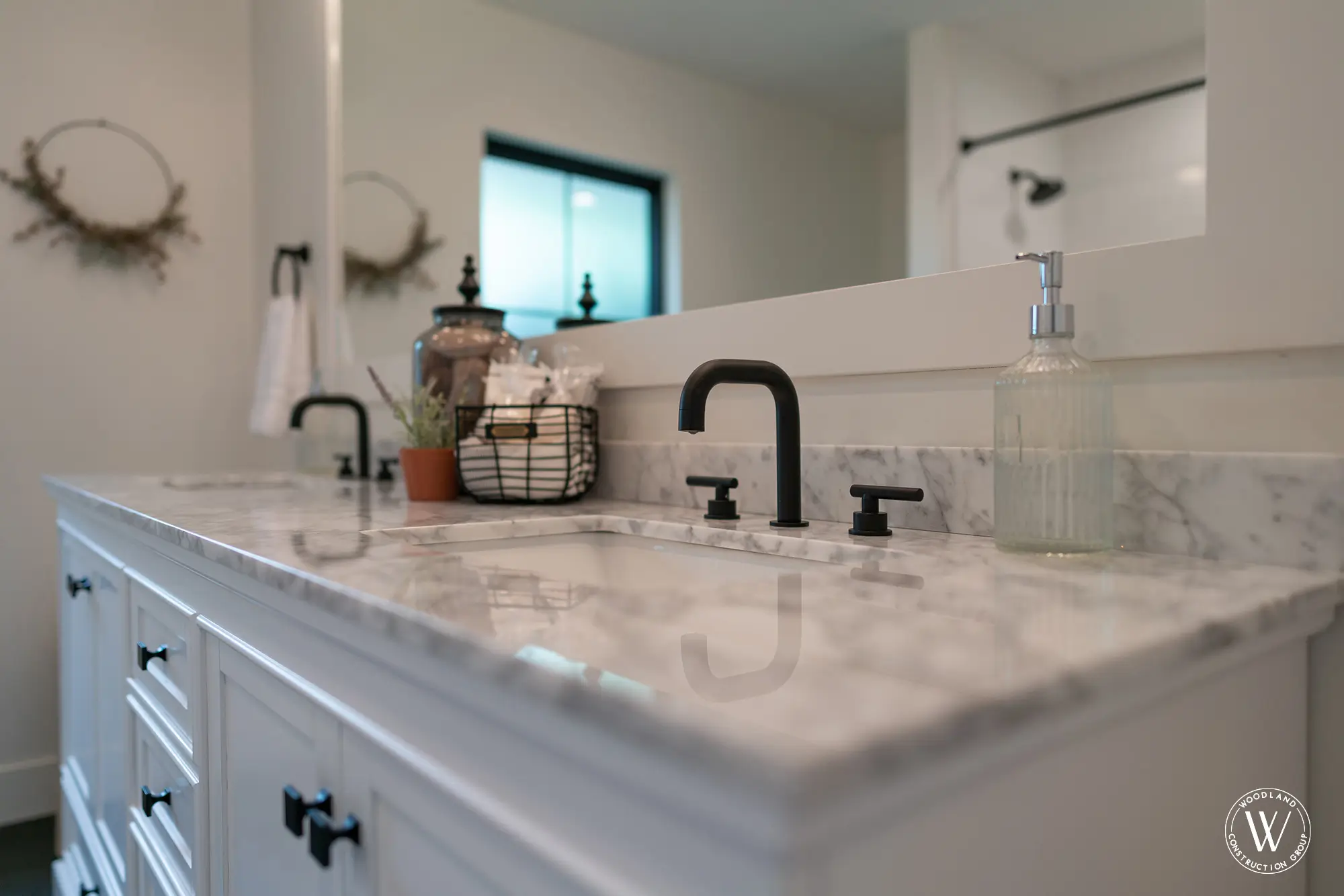 Whitepine bath vanity detail with a marble top, black widespread faucets and a framed mirror
