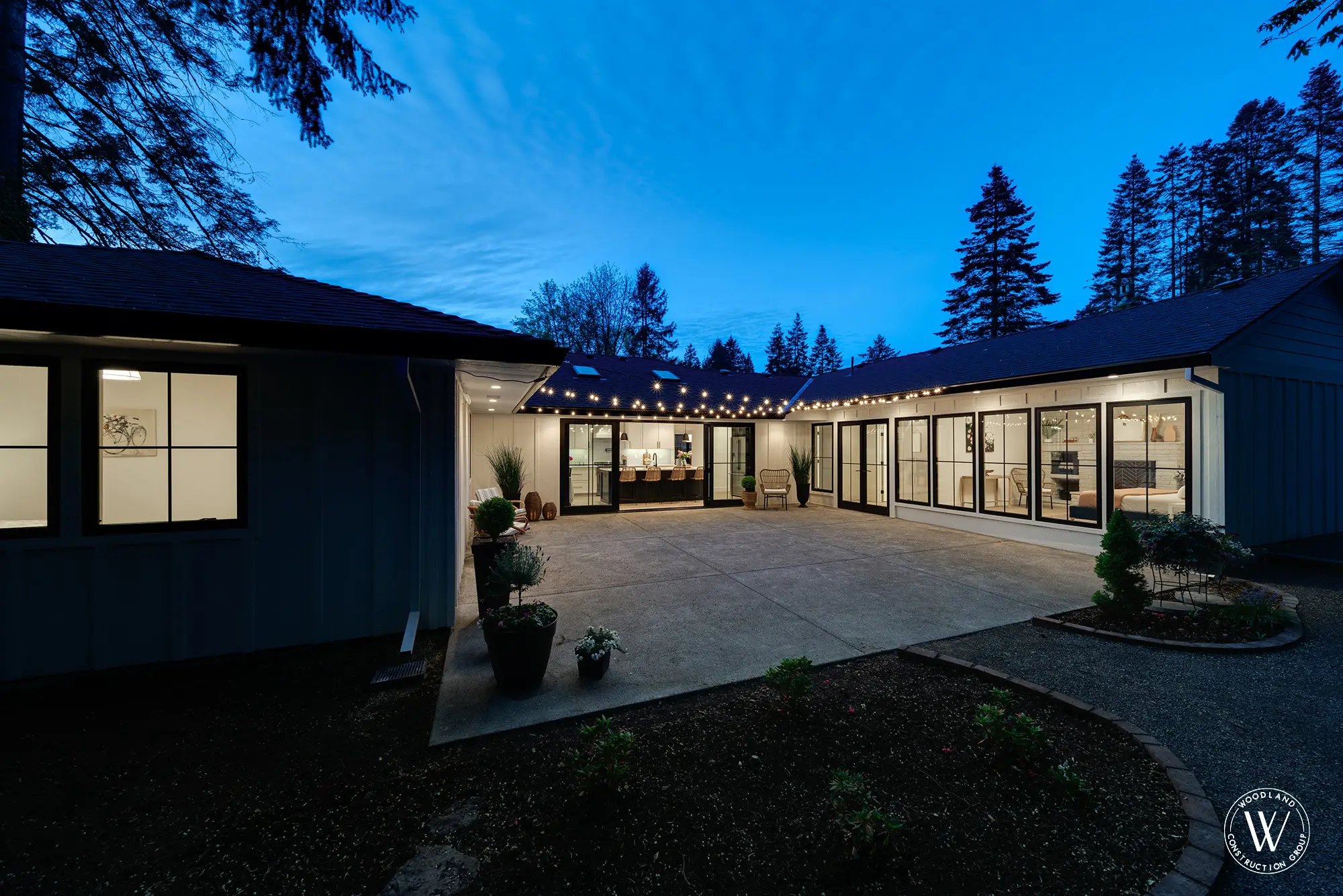 U-shaped Whitepine ranch wrapped around the courtyard at dusk, kitchen and primary suite lit beyond the glass