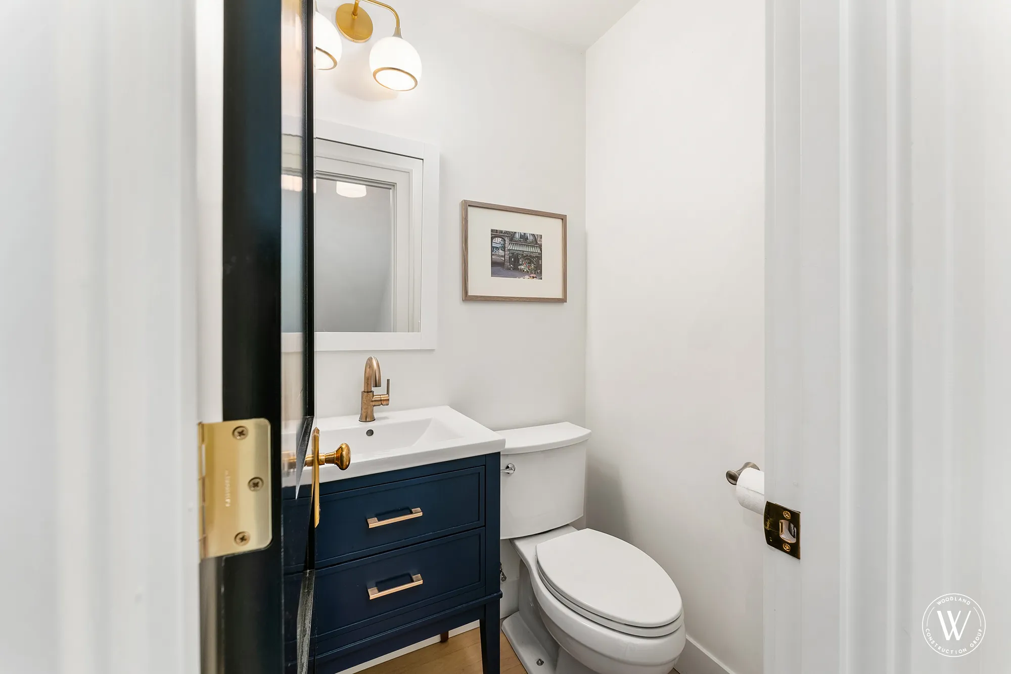 Berkshire powder room with a navy vanity, brass faucet and framed print off the entry