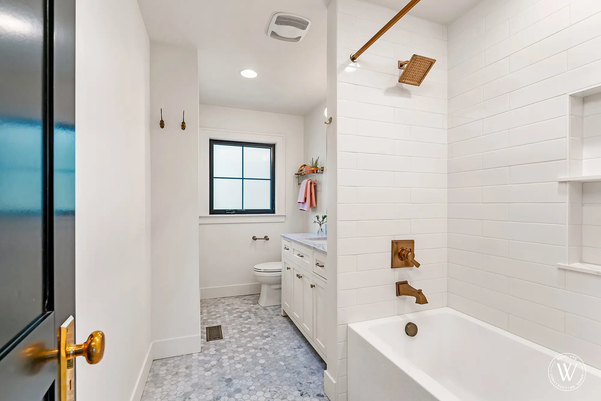 Berkshire hall bath with white subway-tiled tub and shower, brushed-brass fixtures and a marble hex-tile floor