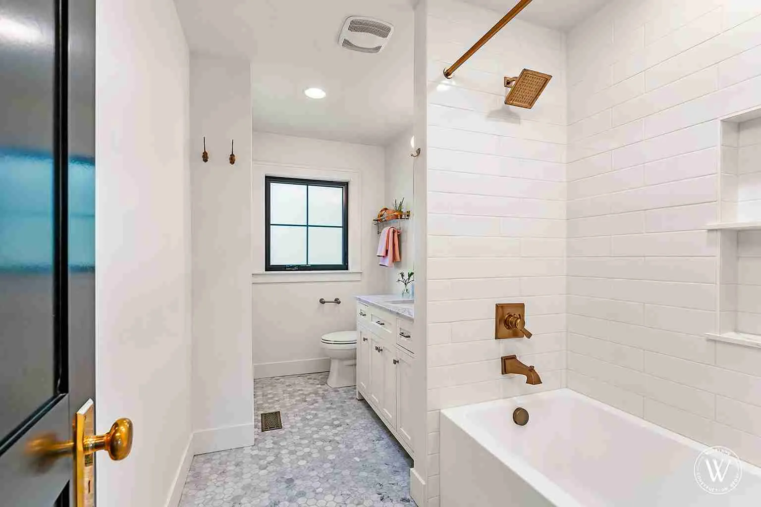 Berkshire bathroom after remodel, white subway-tiled tub and shower with aged-brass fixtures over a marble hex-tile floor, Portland Oregon